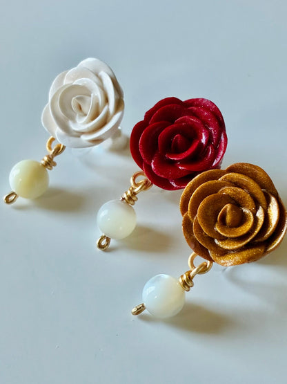 Three flower-shaped earrings in white, red, and gold on a white background